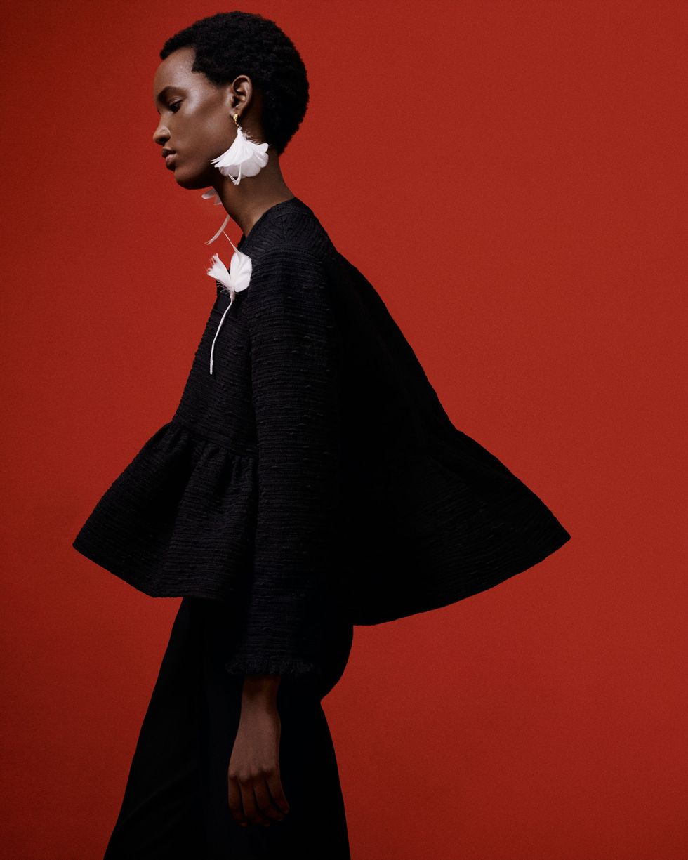 a woman in a black cape and white flower earrings