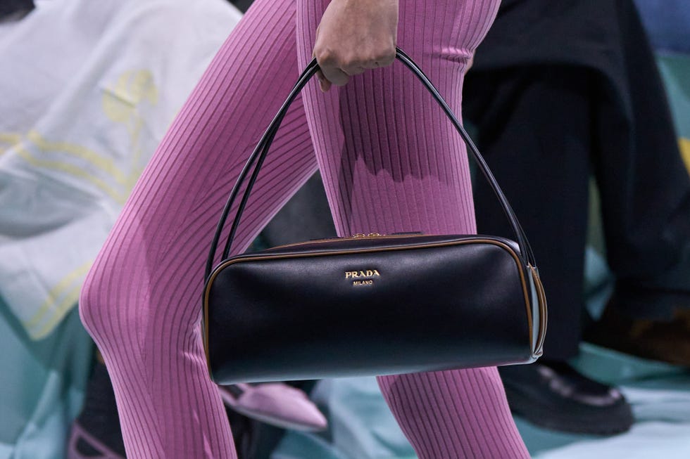 a fashionable individual holding a prada handbag while wearing pink ribbed leggings