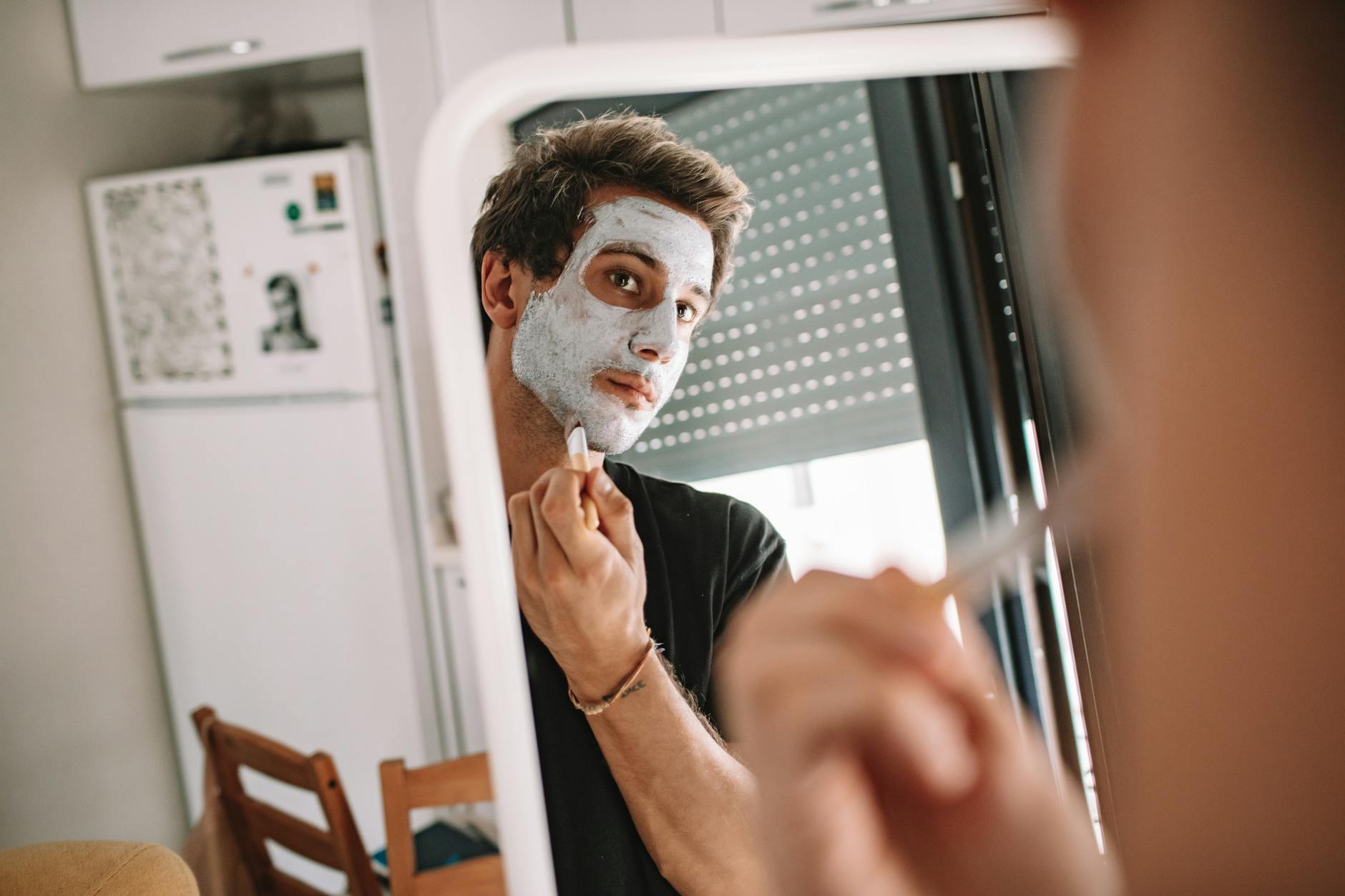 Young man applying skincare product to his face in modern bathroom setting
