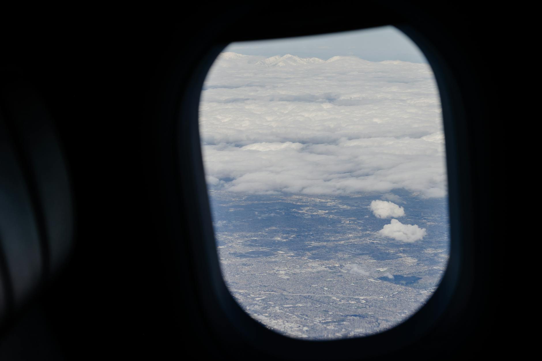 View through airplane window showing clouds below during flight travel