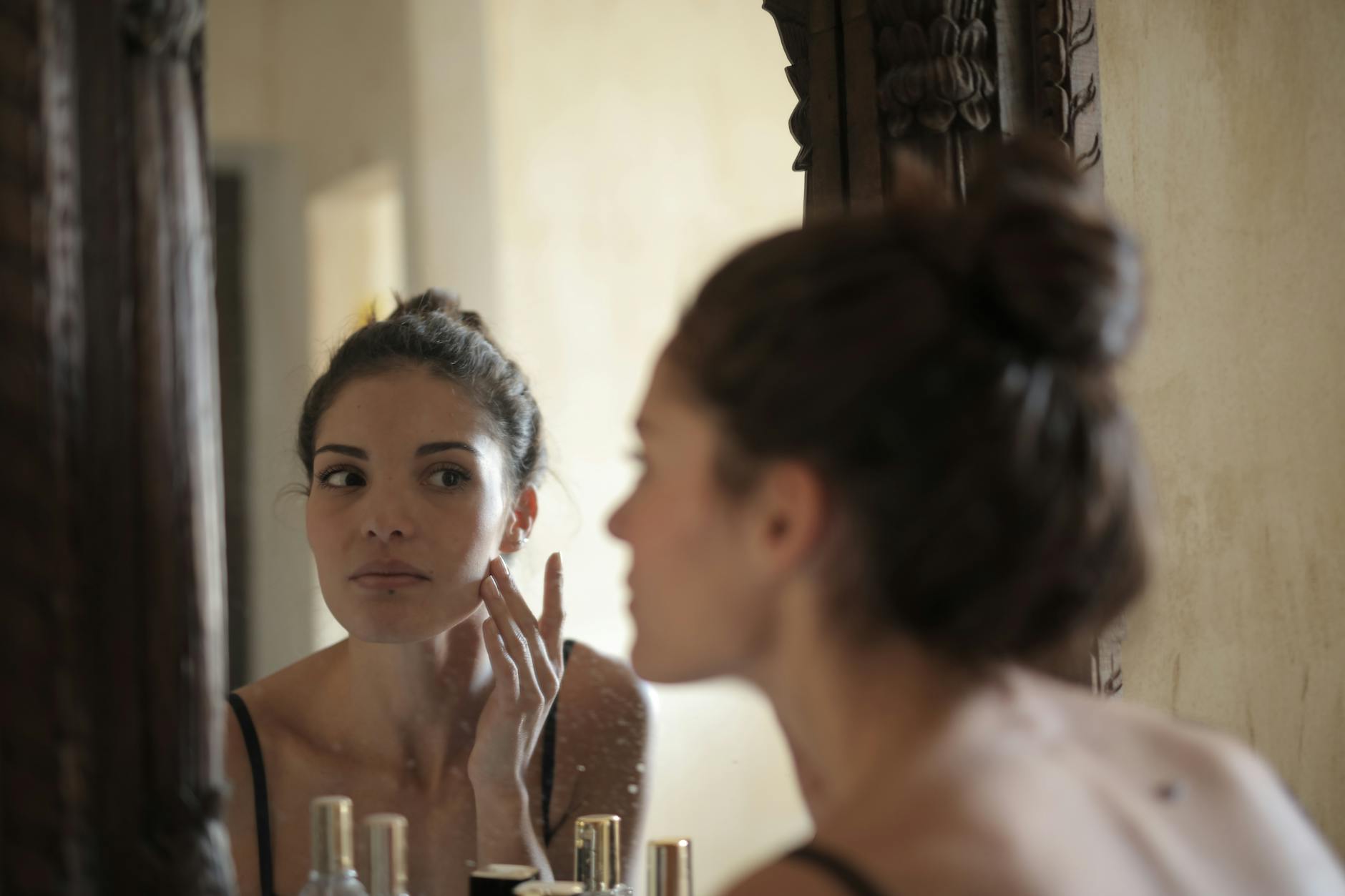 Woman applying probiotic skincare product to her face in bathroom mirror