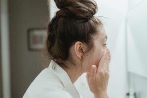 Person applying skincare product to face in bathroom mirror