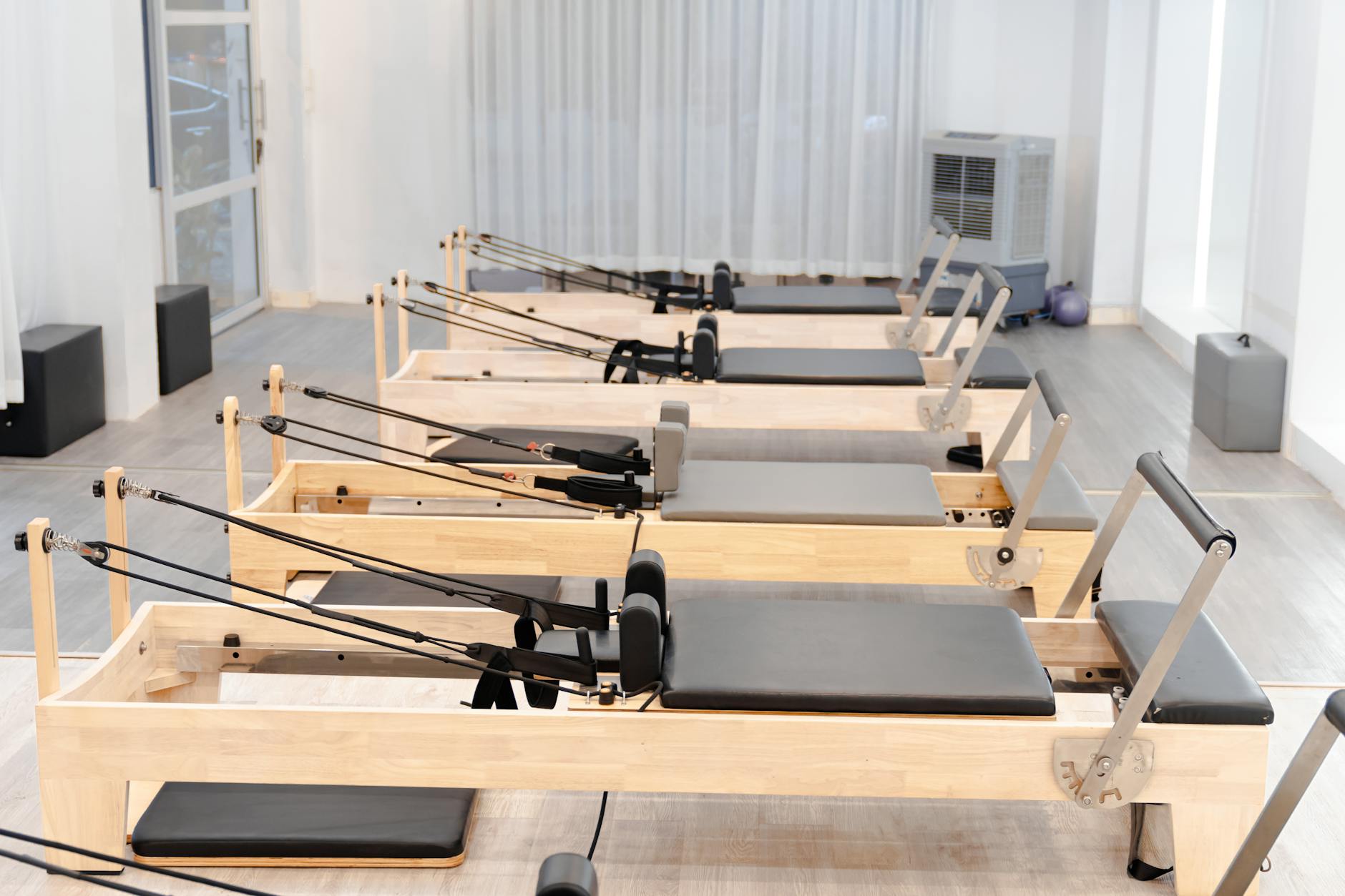Woman in fitted neutral activewear standing near a pilates reformer machine in a bright studio
