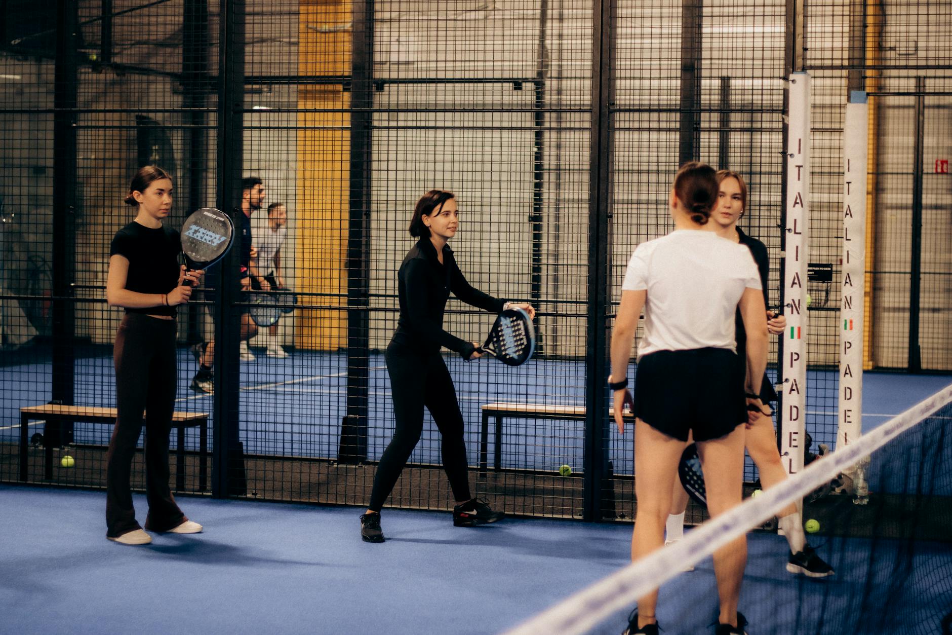 Players on a glass-walled padel court wearing casual athletic clothing
