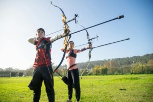 Person practicing archery outdoors wearing structured vest and arm guard