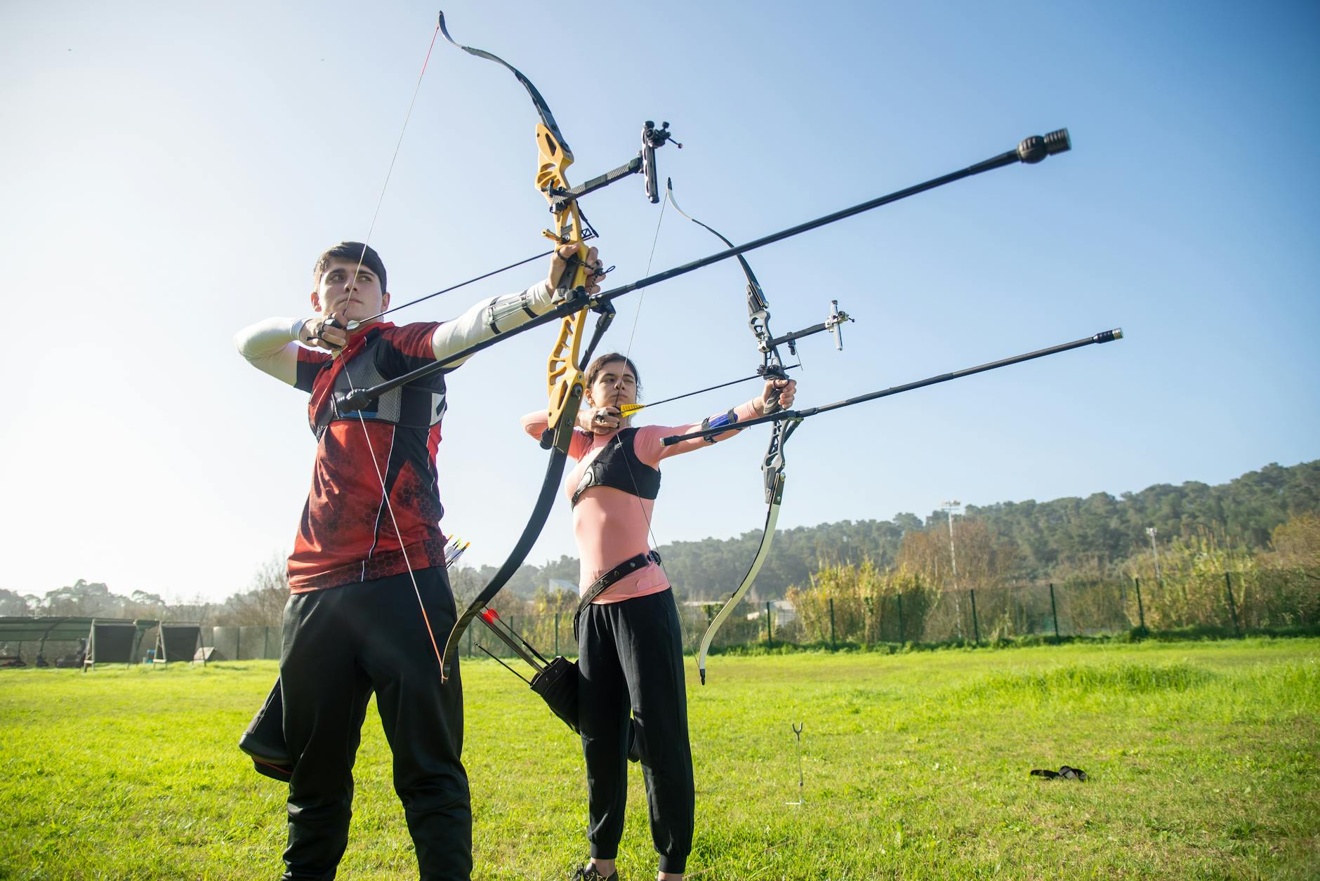 Person practicing archery outdoors wearing structured vest and arm guard
