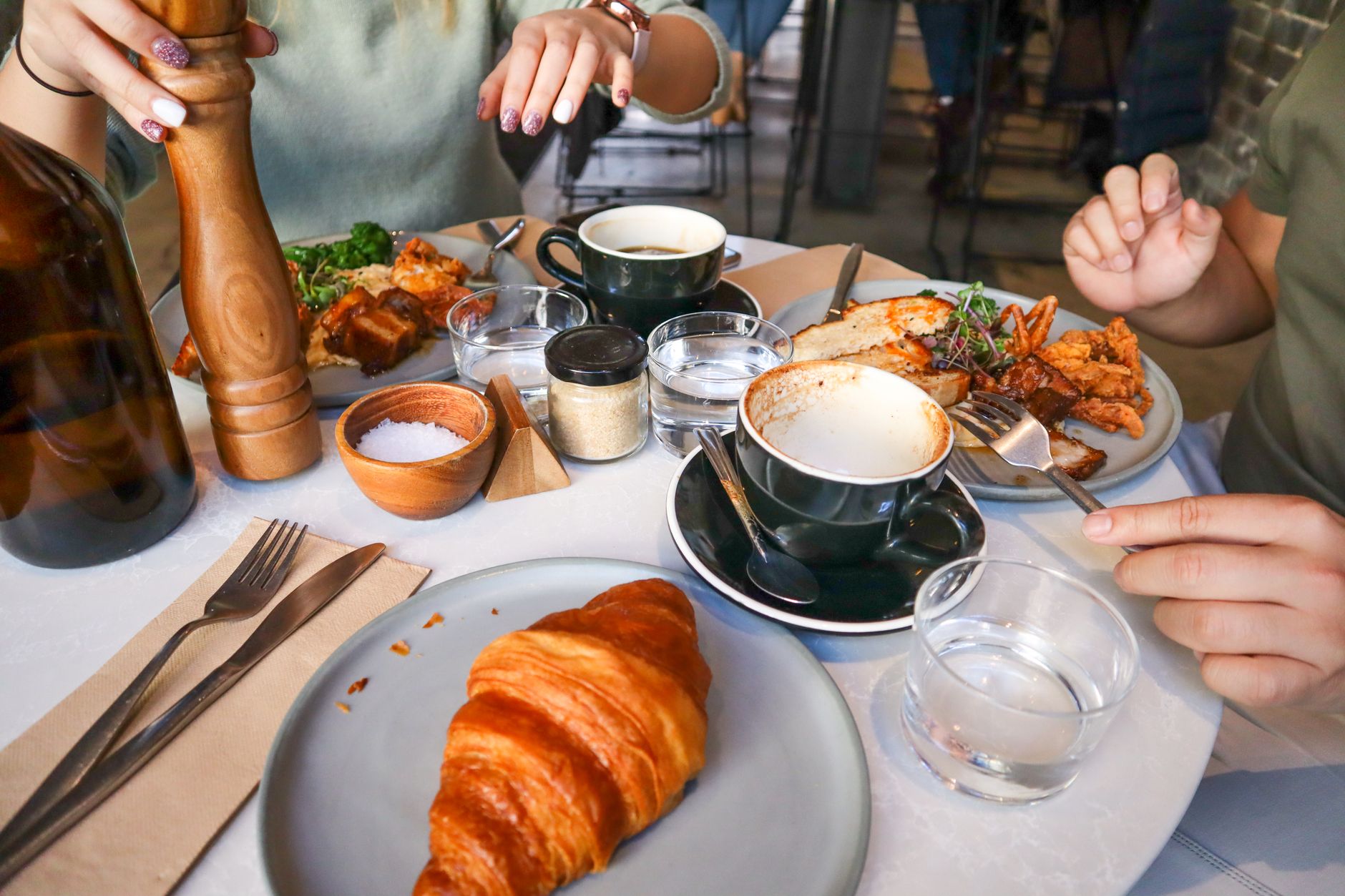 Woman in minimal activewear seated at a sunlit cafe table with a coffee and structured tote bag