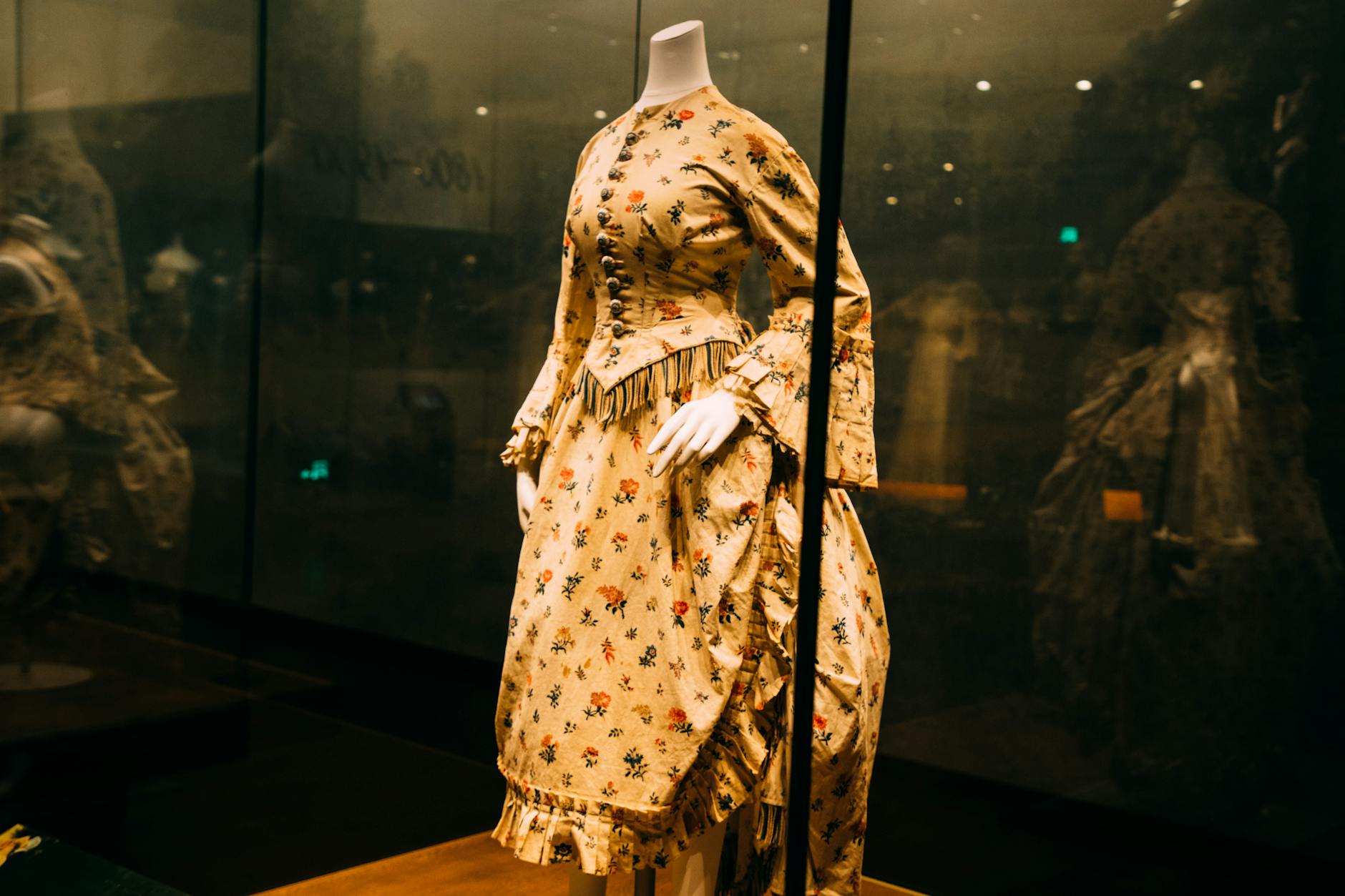 Museum gallery displaying vintage couture pieces behind glass cases with informational placards