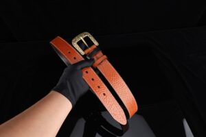 Close-up of a wide leather weightlifting belt with a heavy-duty prong buckle on a dark surface