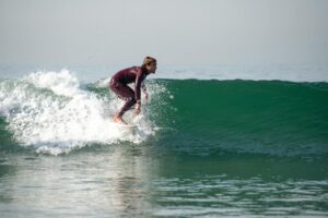 Person wearing a long-sleeve surf rash guard at the beach with board in hand