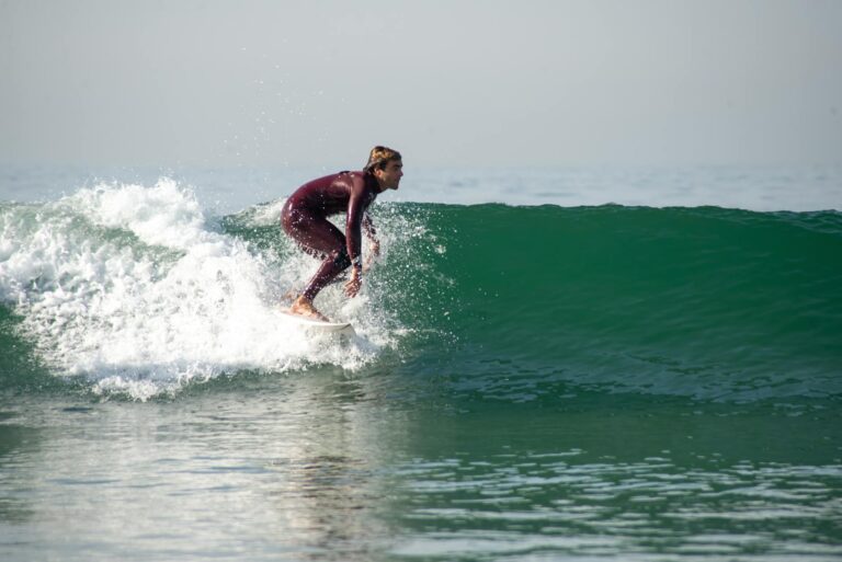 Person wearing a long-sleeve surf rash guard at the beach with board in hand