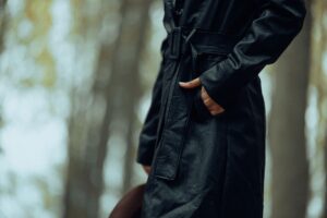 A person wearing a long waxed cotton coat outdoors, evoking equestrian workwear style