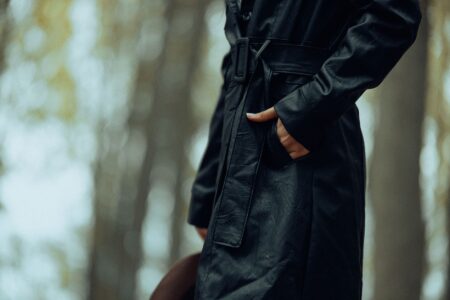 A person wearing a long waxed cotton coat outdoors, evoking equestrian workwear style