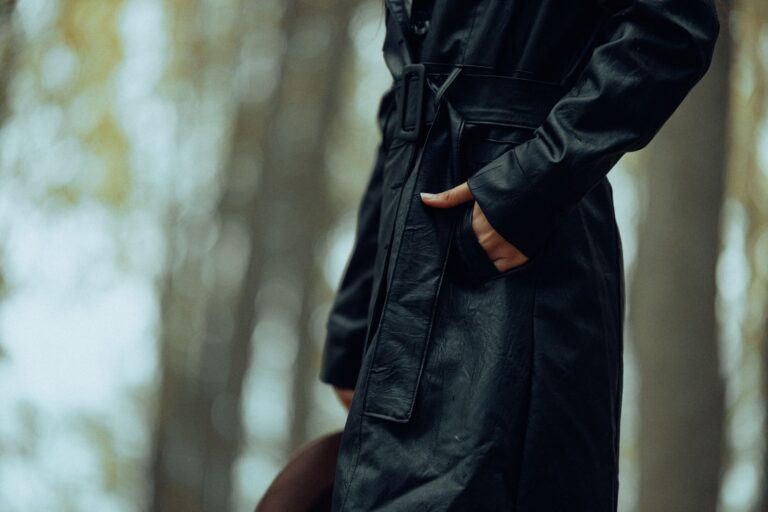 A person wearing a long waxed cotton coat outdoors, evoking equestrian workwear style