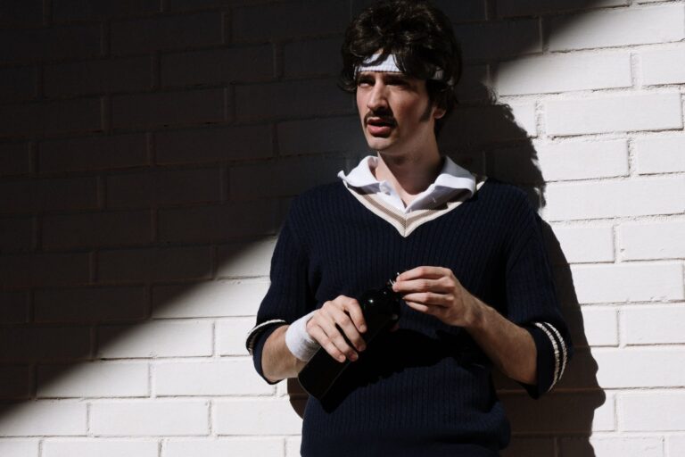 Polo Club Cricket Sweaters Are Creeping Into Off-Duty Tailoring A man wearing a cream cable-knit V-neck sweater layered over a collared shirt with tailored trousers