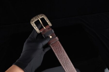 Wide leather belt with prominent brass buckle laid flat on a wooden surface