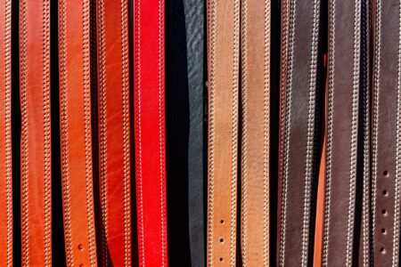 Close-up of a handcrafted leather belt with distinctive loop hardware laid flat on a wooden surface