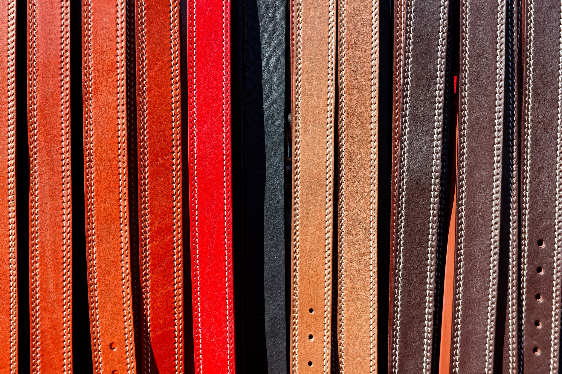 Close-up of a handcrafted leather belt with distinctive loop hardware laid flat on a wooden surface