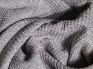 Close-up of quilted wool fabric with geometric stitching pattern in natural oatmeal tones