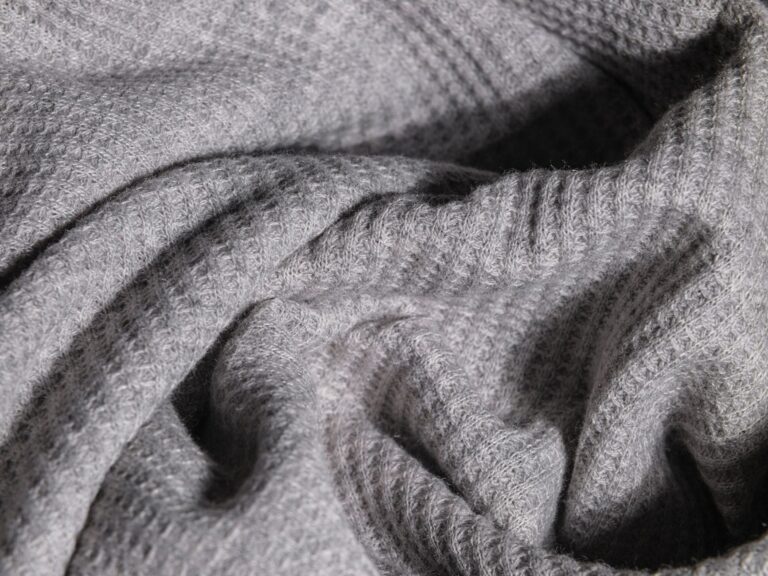 Close-up of quilted wool fabric with geometric stitching pattern in natural oatmeal tones