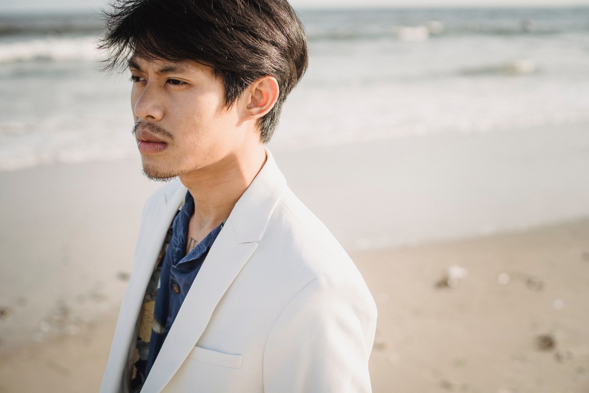 Man wearing an unstructured cream suit with a collarless shirt and minimal accessories