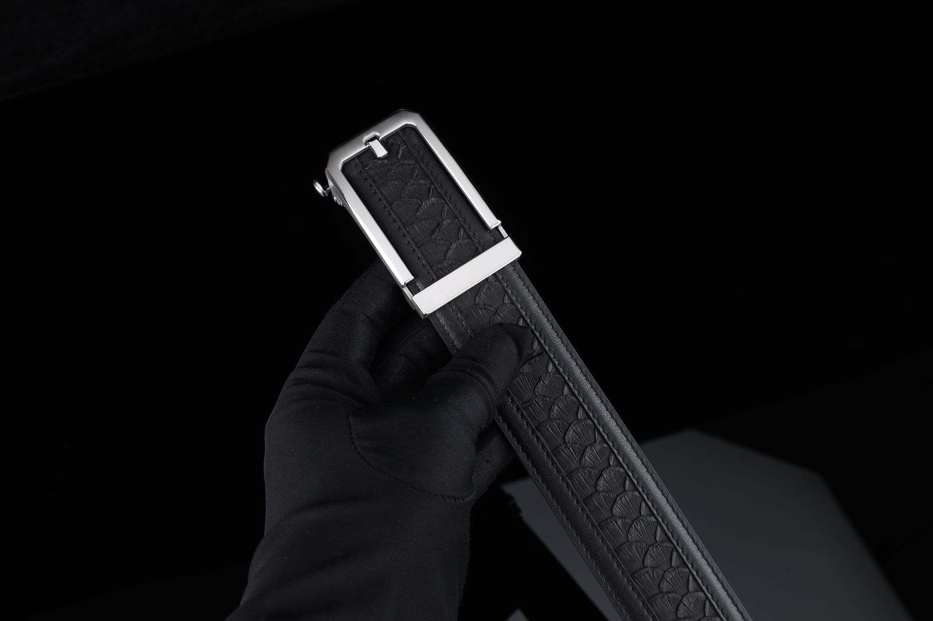 Structured wide leather belt with heavy-gauge metal buckle worn over tailored outerwear