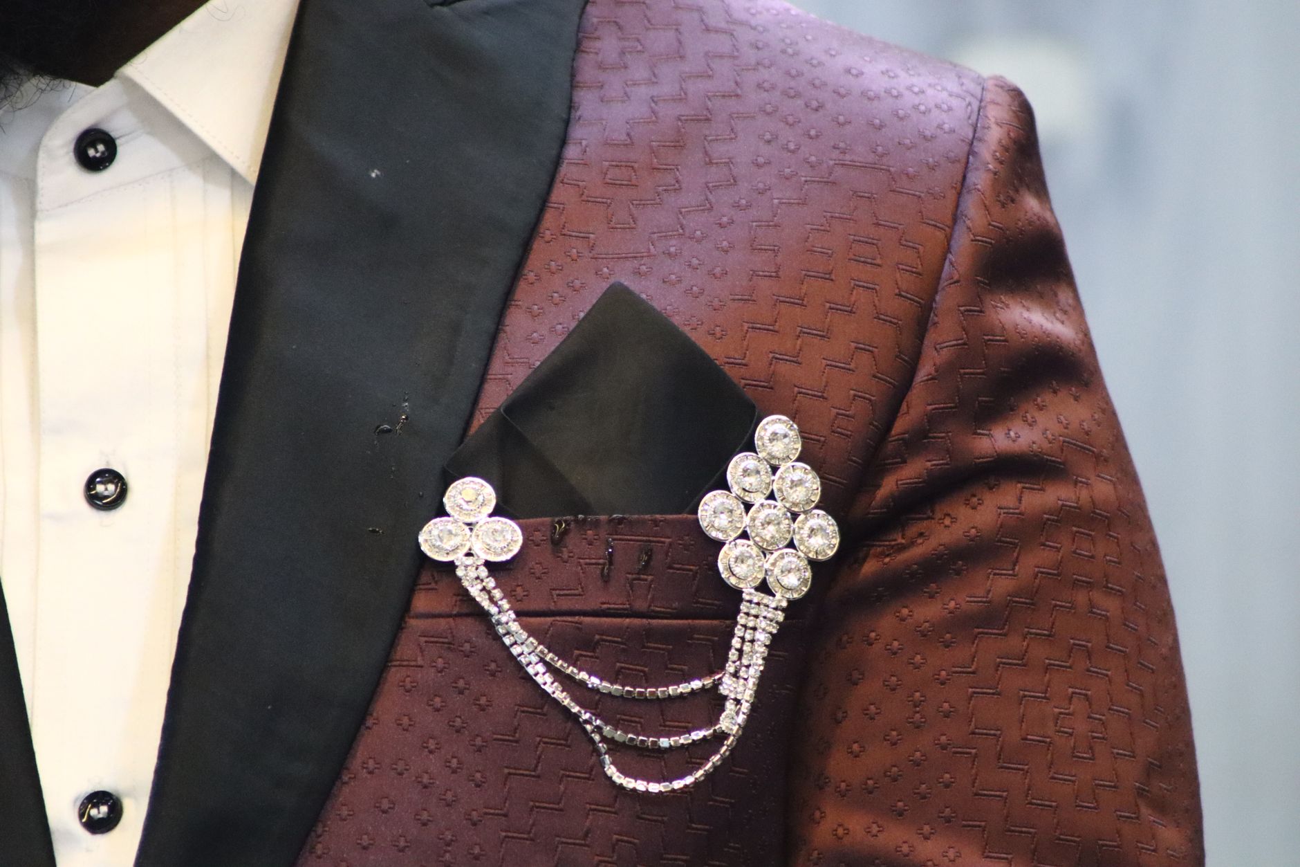 Close-up of a minimalist blazer lapel with a small metal pin detail on tailored suiting fabric