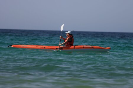 Close-up of a kayak paddle showing offset feathered blade angles above calm flat water