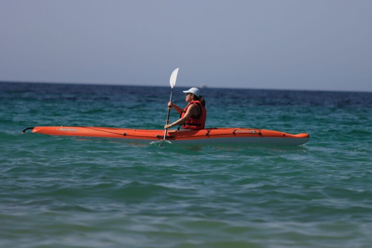 Close-up of a kayak paddle showing offset feathered blade angles above calm flat water