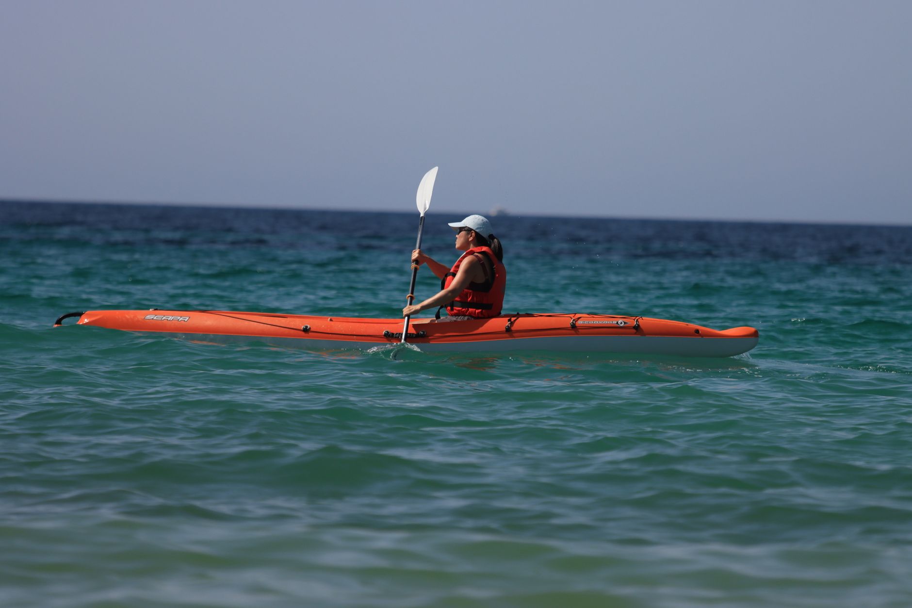 Close-up of a kayak paddle showing offset feathered blade angles above calm flat water