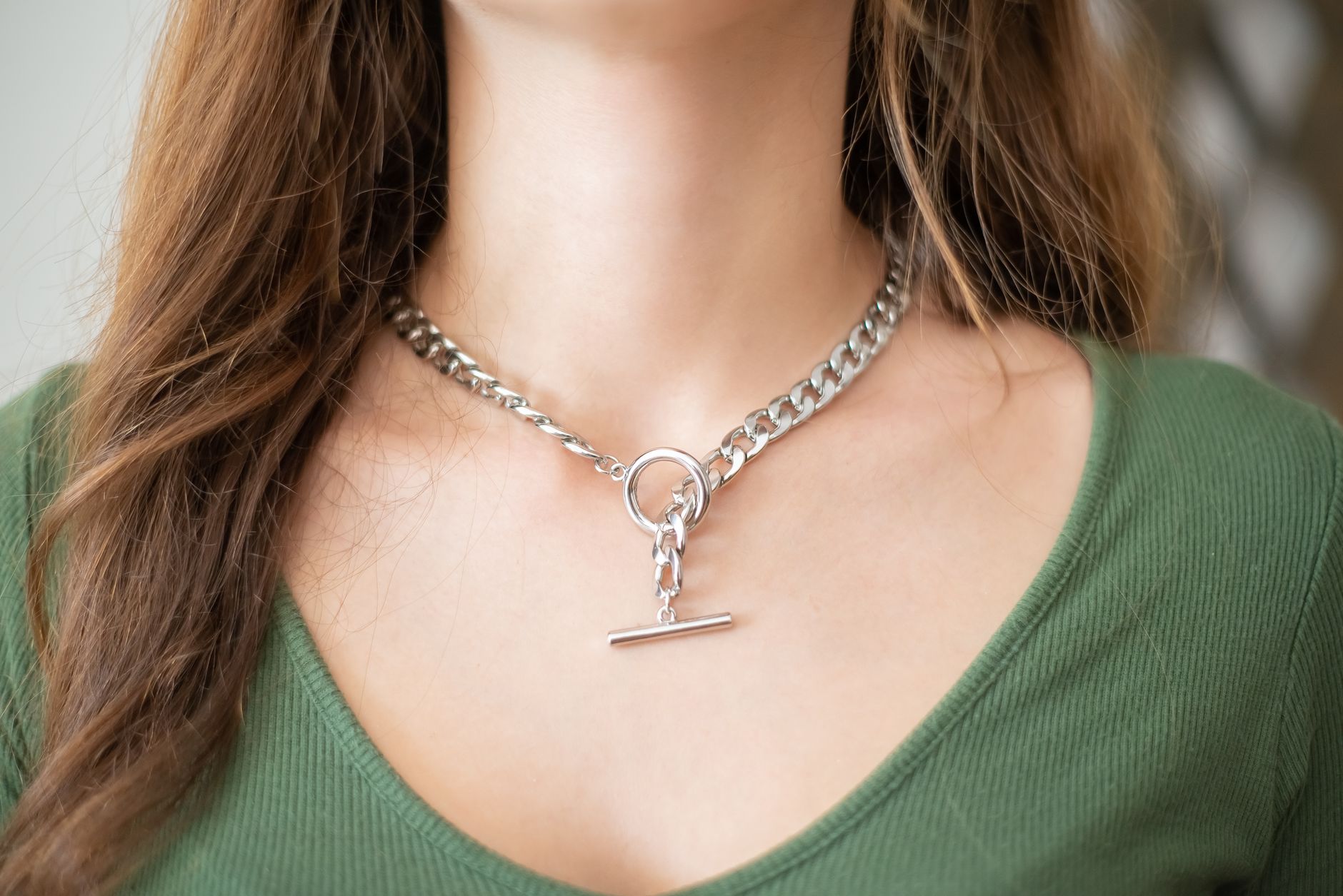 Close-up of a minimalist silver chain necklace with geometric link detailing laid flat on a light surface