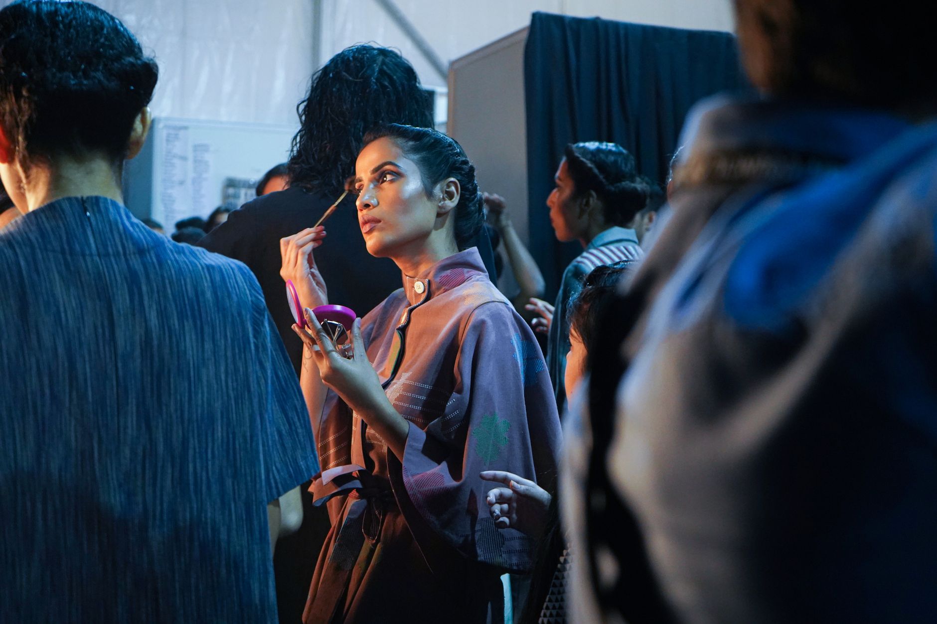 Backstage at a fashion show with garments on rails showing structured skirt silhouettes in heavy fabric
